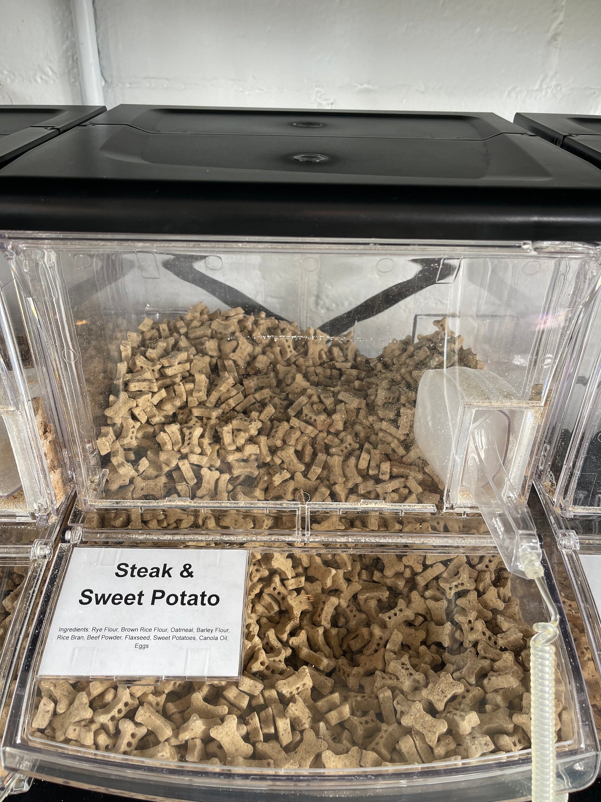 Assorted bulk dog treats displayed in clear containers showing various shapes, sizes and natural ingredients.