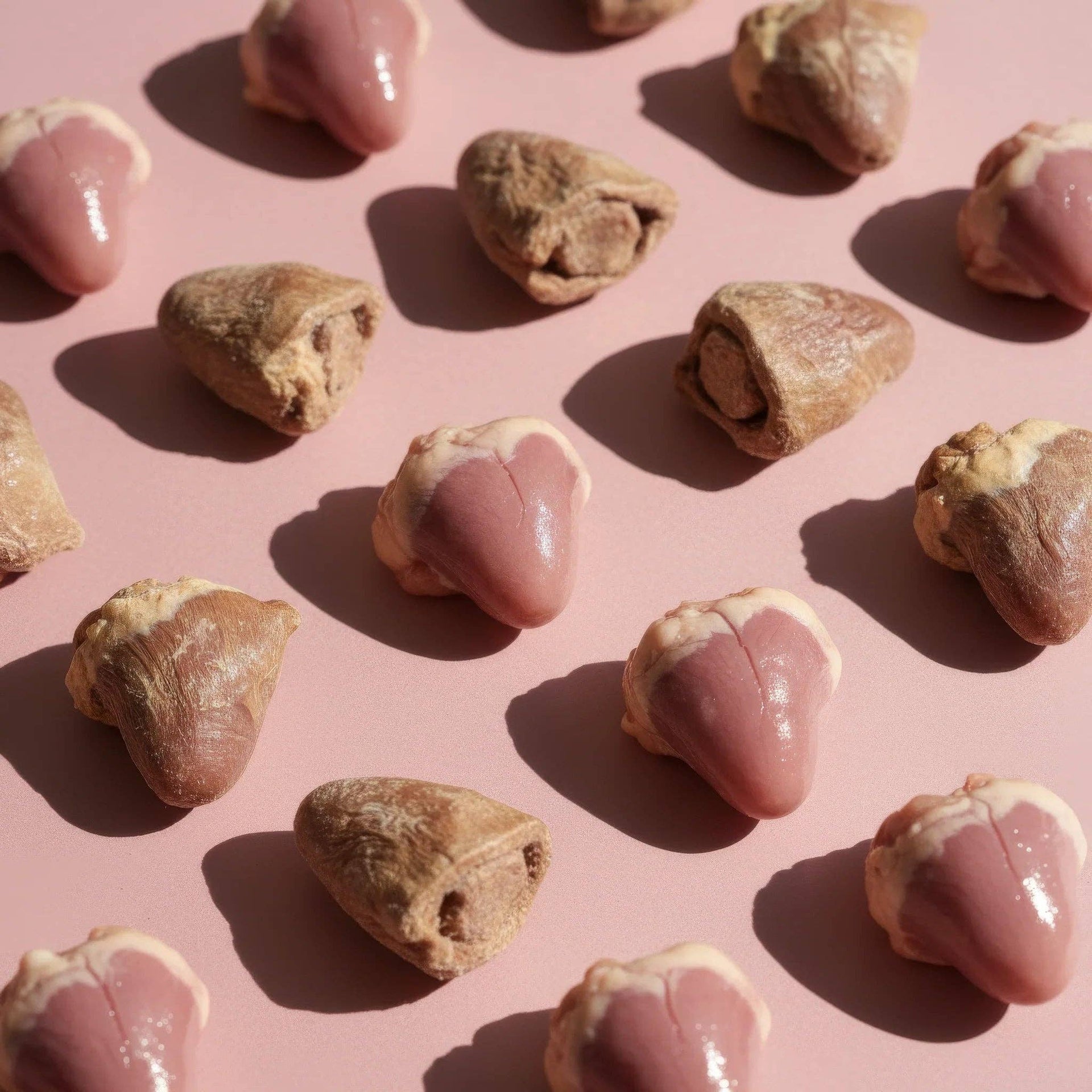 Dog Dish Max & Bella freeze-dried chicken heart pet treats arranged in a grid on a soft pink background