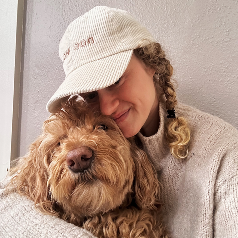Dog Dish ivory corduroy Dog Mom baseball cap worn by a woman hugging her golden doodle dog