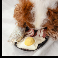 Dog Dish Lambwolf breakfast enrichment toy with egg, bacon, and sausage being sniffed by a brown and white dog.
